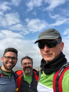 3 males looking at the camera with blue sky above.