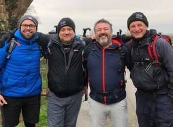 4 males with arms around each other, dressed for a walking challenge
