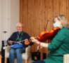 A patients enjoys playing an instrument whilst smiling at the music therapist, who is playing the viola