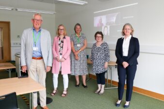 Five Trustees meeting in person with another on screen behind joining the group 'virtually'