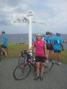 Female cyclist standing in front of John O Groats sign with her bike