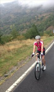 Female cyclist riding along road with green trees behind