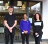Colleagues who work in the Hospice's Bistro smile as they stand on decking with the inside dining area behind