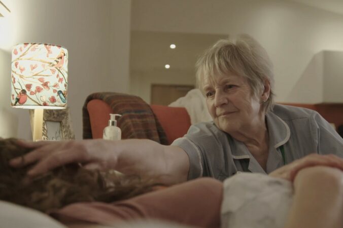 Female nurse stroking a patients head who is laying in bed