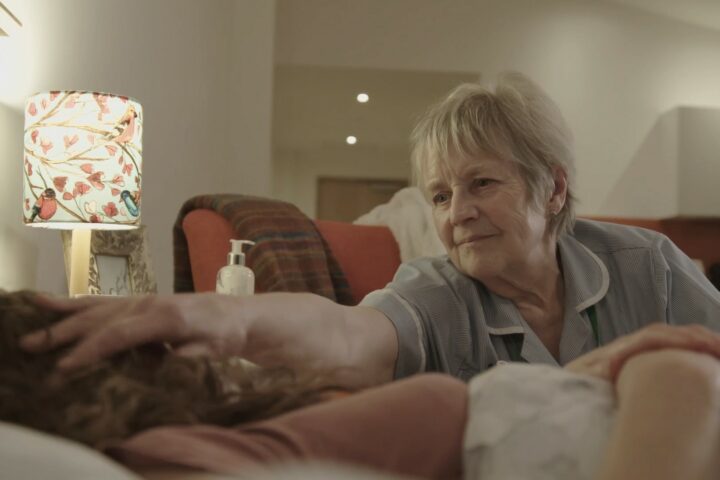 Female nurse stroking a patients head who is laying in bed