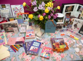 Books, games, flowers displayed on a blue table cloth