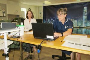 2 nurses, 1 in a blue uniform look at the laptop in the Living Well Service room 