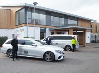 2 silver taxis outside Hospice Building with 2 males and a female