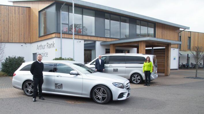 2 silver taxis outside Hospice Building with 2 males and a female
