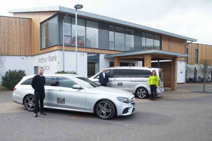 2 silver taxis outside Hospice Building with 2 males and a female