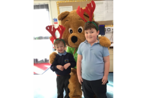 Life sized bear and 2 mboys in school uniform wearing red antlers