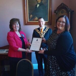 2 females holding a certificate with male Mayor behind