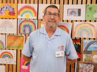 Male with glasses wearing a blue nurse uniform smiling at the camera