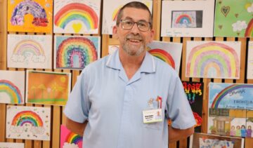 Male with glasses wearing a blue nurse uniform smiling at the camera