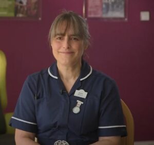 Female wearing a dark blue nurse uniform sitting in front of a pink wall