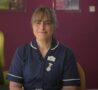 Female wearing a dark blue nurse uniform sitting in front of a pink wall