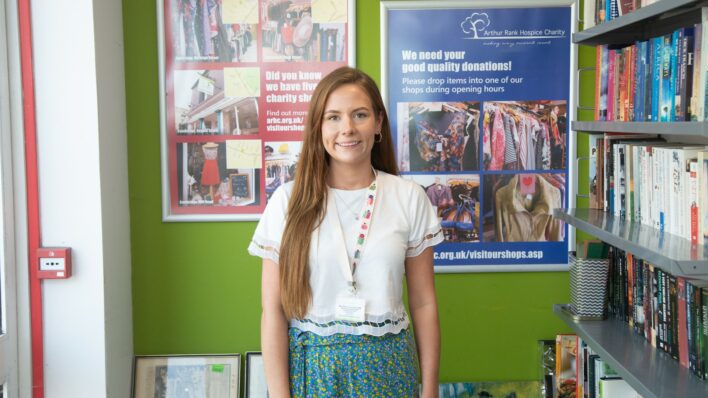 Female smiling at the camera standing in front of a green wall with red and blue posters on the wall