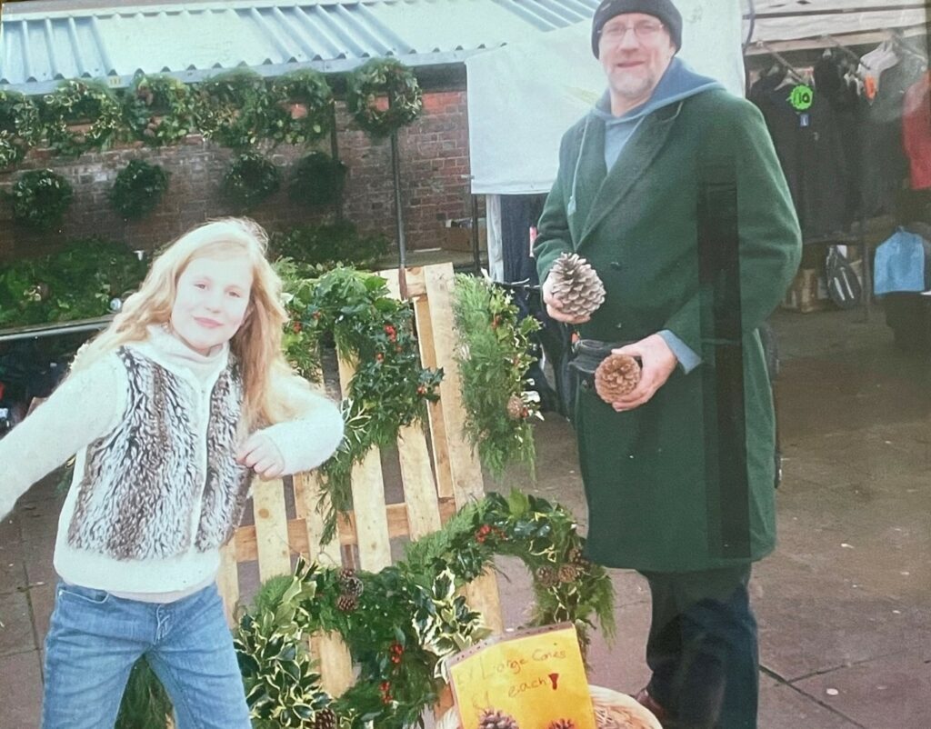 Young girl and her dad wearing a green coat and hat looking at the camera