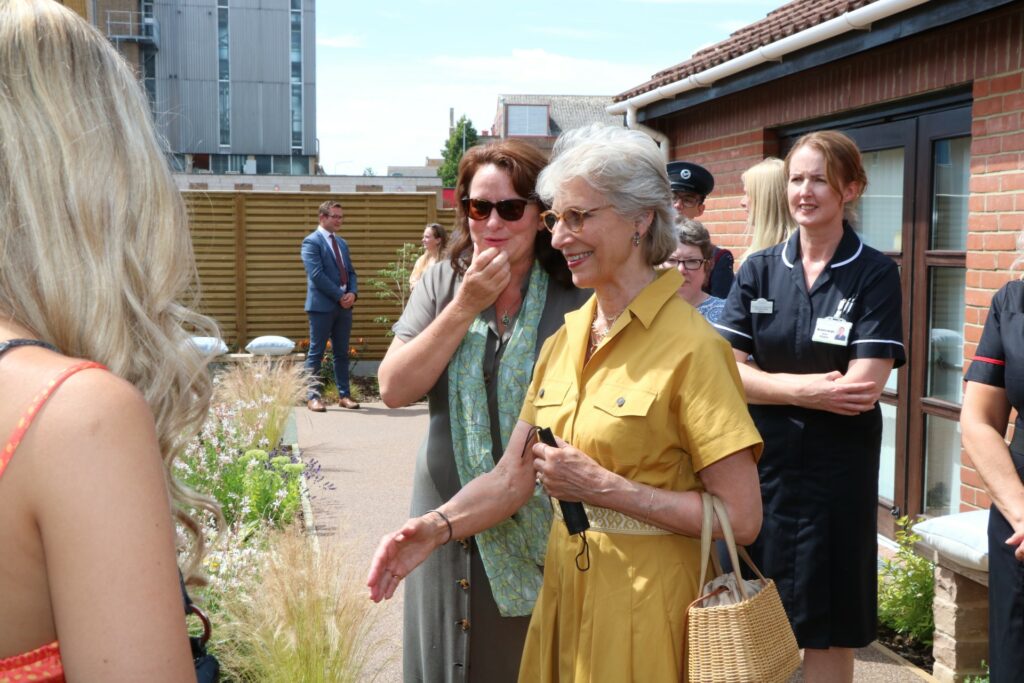 HRH Duchess of Gloucester yellow dress smiling in garden shaking hands nurse in background 