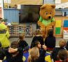 Life sized bear wearing green tshirt talking to school children