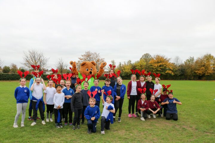Group of children in blue school sweatshirts wearing red antlers in a group in on the school playing field