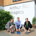 2 women and 1 man trainers Arthur Rank Hospice Charity sign