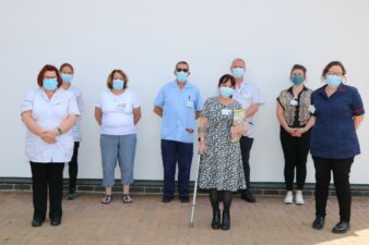 Females some in nurse uniforms spacialy distanced near a white wall
