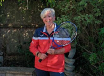 female holding tennis racket smiling at the camera