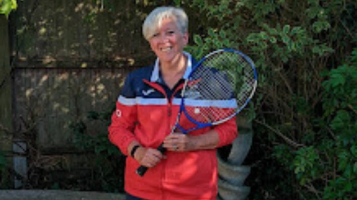 female holding tennis racket smiling at the camera
