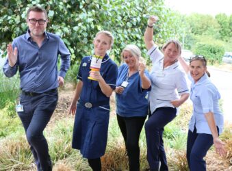 Male and 4 females wearing clinical uniforms smile to the camera