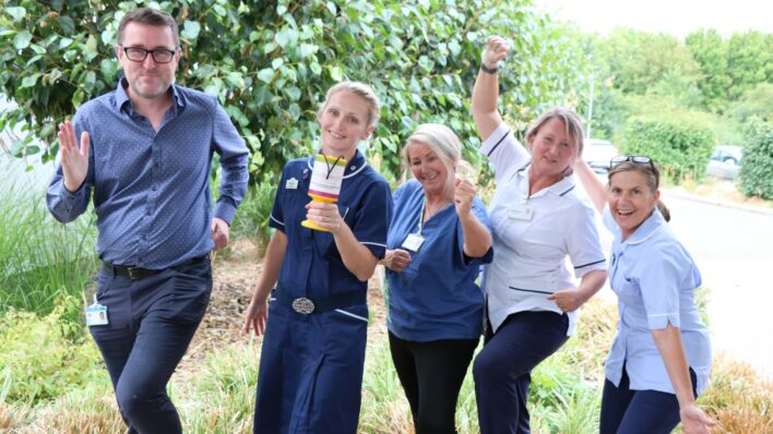 Male and 4 females wearing clinical uniforms smile to the camera