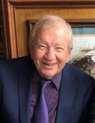 Male smiling at the camera wearing a blue jacket and purple shirt and tie