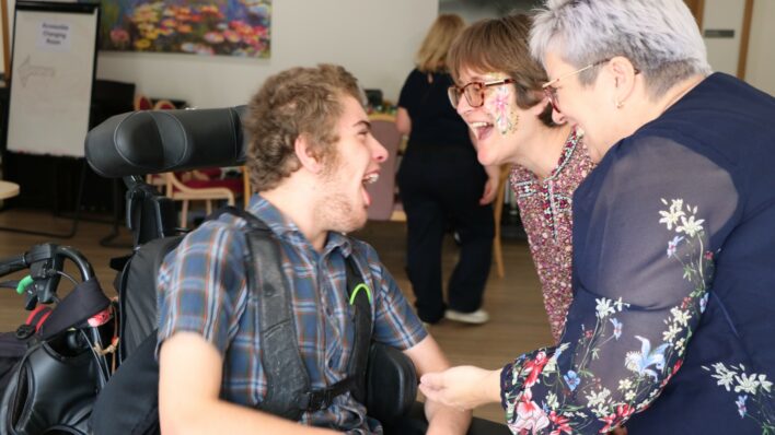 Older boy in a wheel chair laughing at 2 females who are laughing too