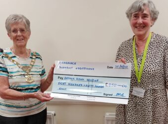 2 females, one with a decorated chain around her neck, holding a large cheque smiling at the camera