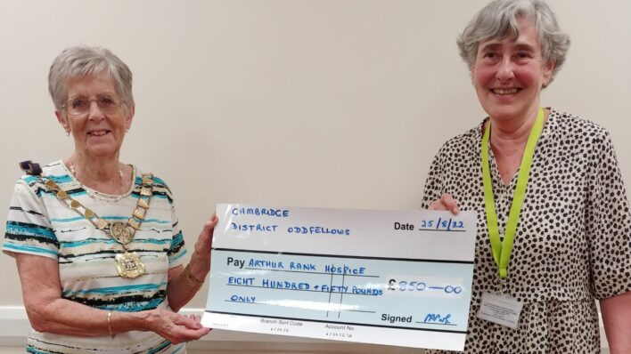 2 females, one with a decorated chain around her neck, holding a large cheque smiling at the camera