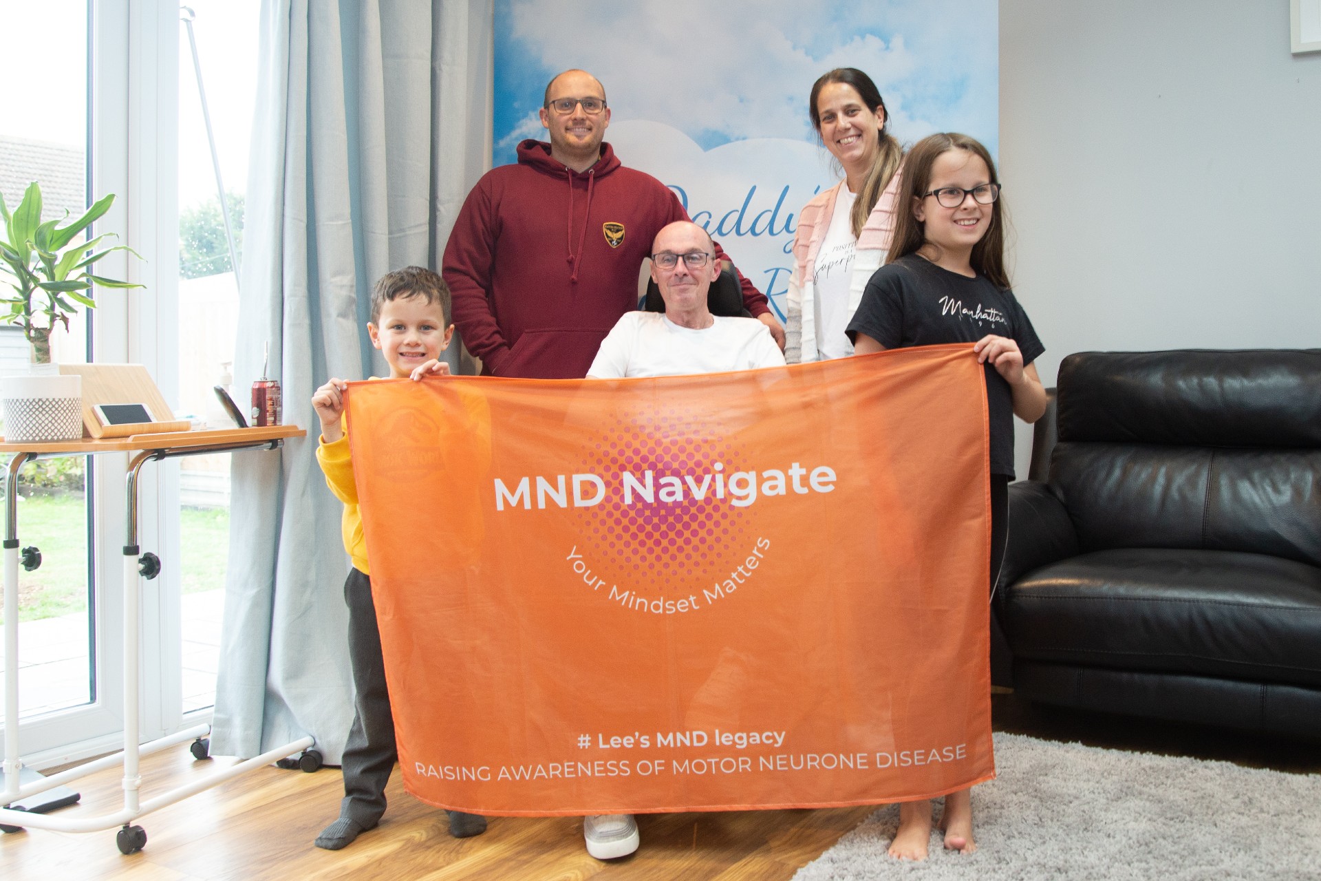 3 adults and 2 children holding an orange banner