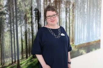 Female with glasses standing in front of a woodland picture