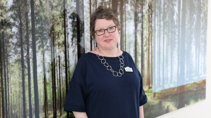 Female with glasses standing in front of a woodland picture