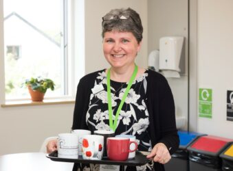 Female smiling at the camera holding a tray of tea cups