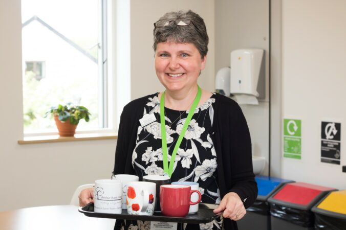 Female smiling at the camera holding a tray of tea cups