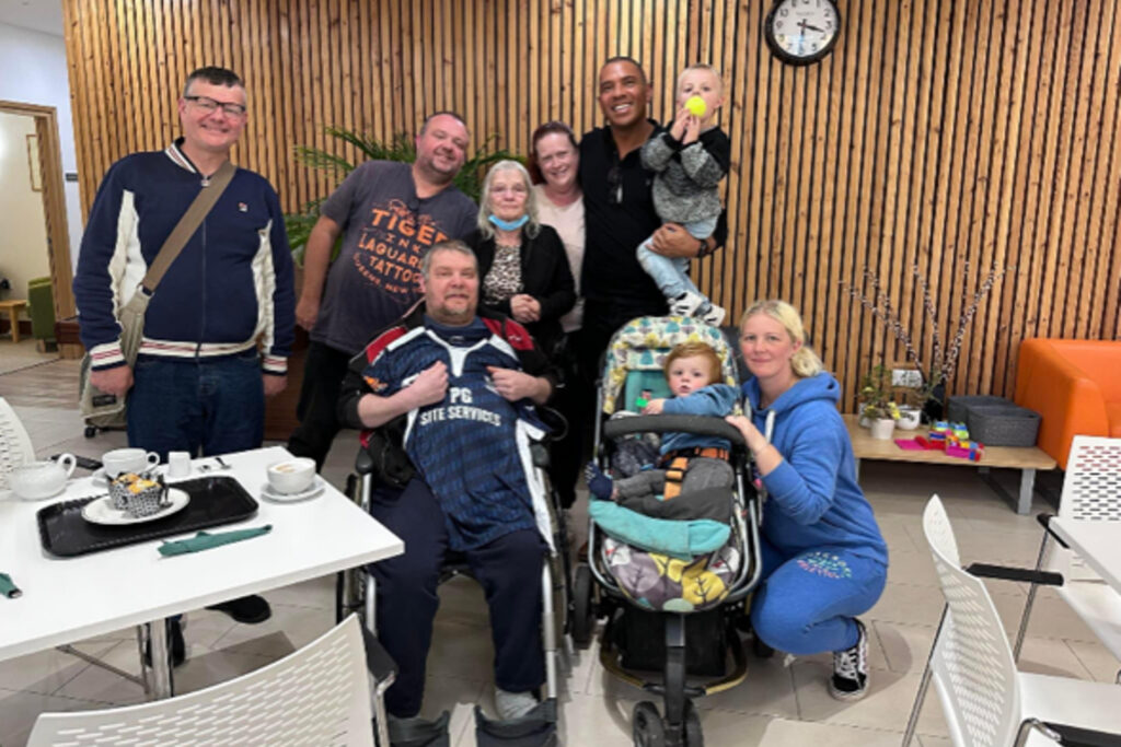Male and females adults and children smile at the camera in a group around a male in a wheelchair