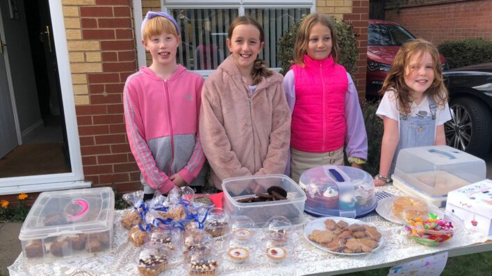 4 young females in front of a table full of homemade cakes