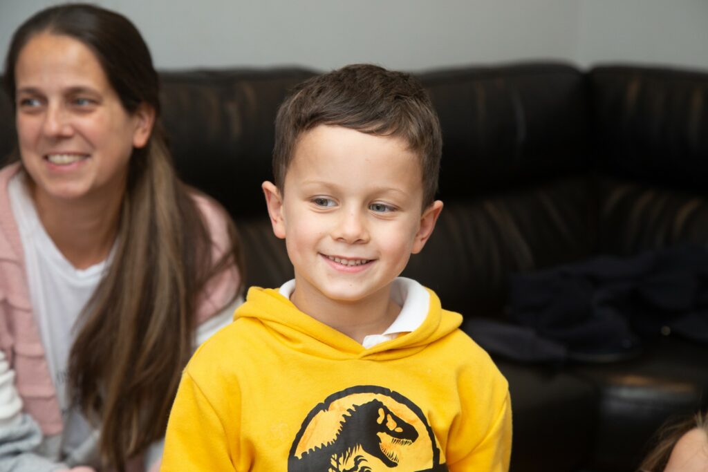 Boy smiling, yellow sweatshirt and female behind