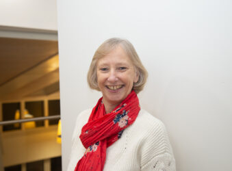 Female smiling at the camera wearing a white jumper and pink scarf