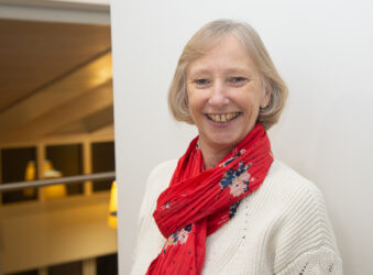 Female smiling at the camera wearing a white jumper and pink scarf