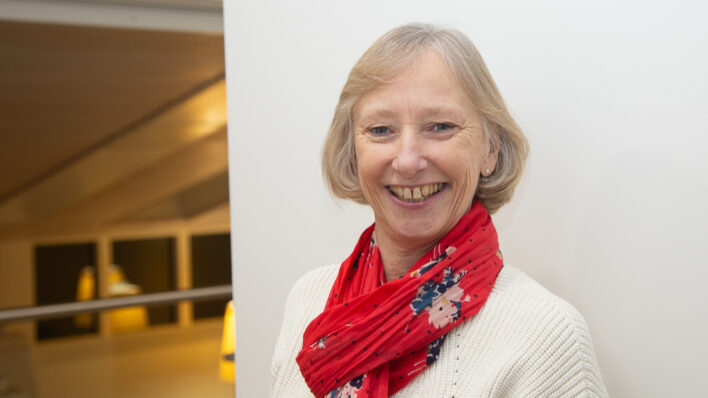 Female smiling at the camera wearing a white jumper and pink scarf