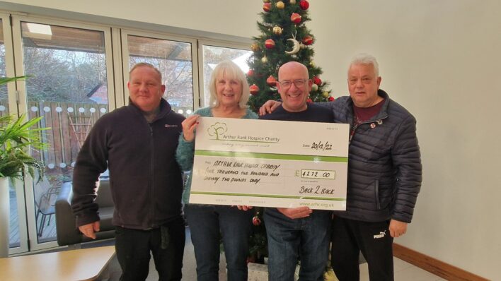 three men one lady holding the cheque in front of Christmas tree