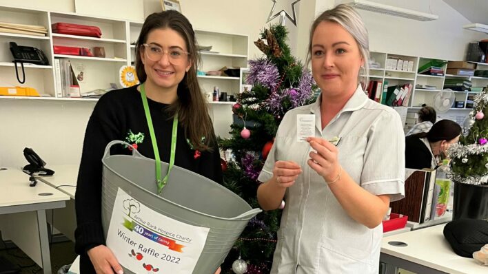 Female and female nurse with Christmas tree behind holding a raffle ticket