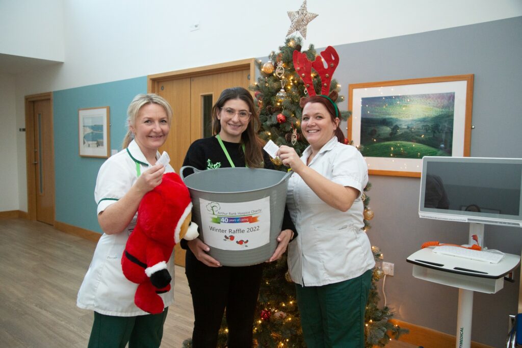 2 nurses and female with big raffle buckets and Christmas tree behind 