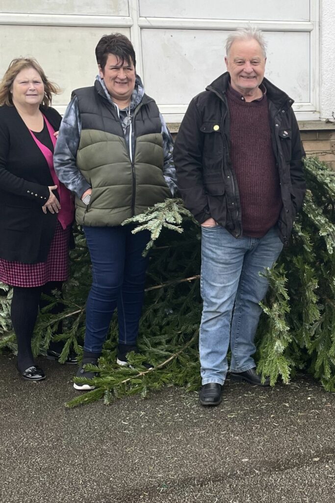 2 females and a male standing near real Christmas trees